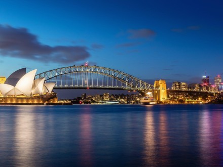 Sydney Harbour Bridge and Opera House at dusk with lights reflecting on water